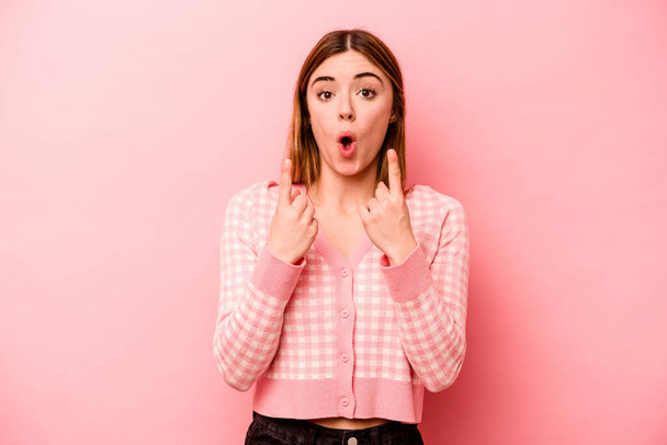 Young caucasian woman isolated on pink background pointing upside with opened mouth. - Foto, Imagem