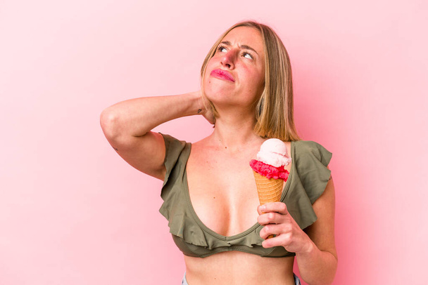 Молодая белая женщина в бикини и с мороженым, изолированным на розовом фоне, трогает затылок, думает и делает выбор. - Фото, изображение