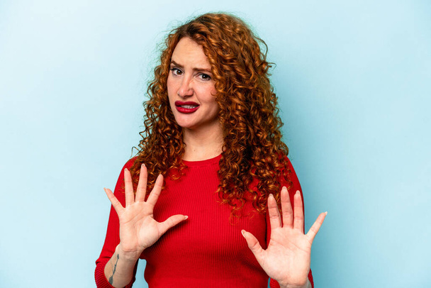 Young ginger caucasian woman isolated on blue background rejecting someone showing a gesture of disgust. - Foto, Imagen