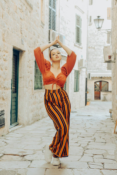 A very beautiful woman poses on the streets of an old city in Europe while traveling. Leisure and vacation in Europe. Beautiful girl with styling - Foto, Bild