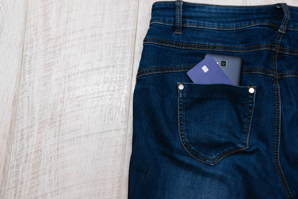 Банківська картка та смартфон у джинсовій кишені на світлому дерев'яному фоні, копіювання місця зліва
. - Фото, зображення