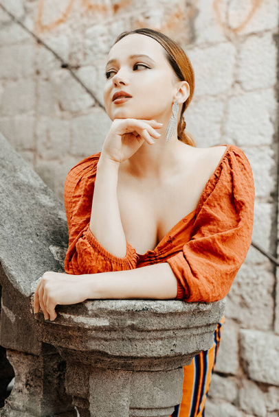 Gorgeous portrait of a beautiful woman in the old city on the stairs. Girl with makeup and hairstyle, long silver earrings posing - Photo, Image