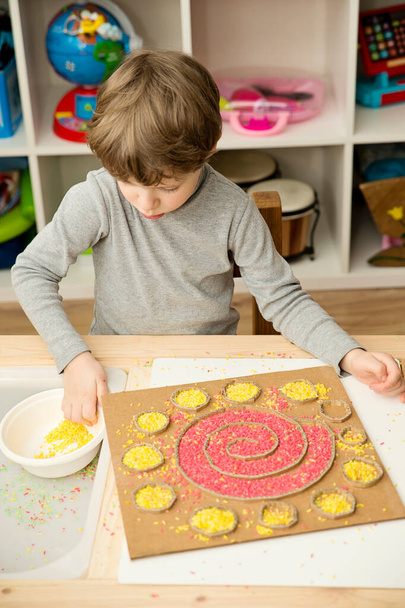 Boy plays with colored rice. Implement for children to develop fine motoric skills through play. DIY toy to learn hand - eye coordination. Montessori type pre school activities at home. - Foto, Imagem