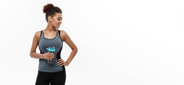 Conceito saudável e Fitness - bela menina afro-americana em roupas esportivas segurando garrafa de água após o treino. Isolado no fundo do estúdio branco
. - Foto, Imagem