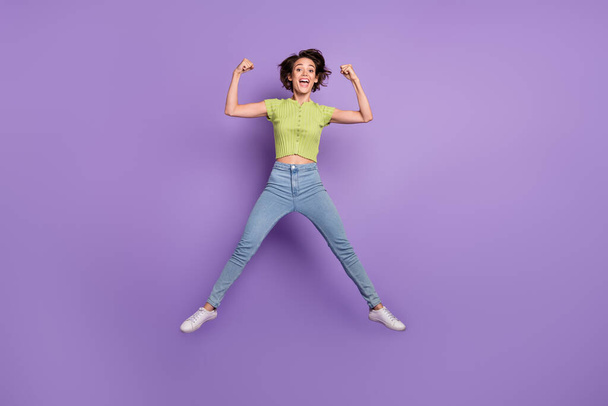 Photo of attractive strong young woman dressed green t-shirt showing muscles jumping high isolated purple color background. - Foto, afbeelding