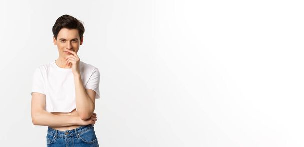 Lgbtq and pride concept. Satisfied young gay man thinking, having an idea and smiling while staring at camera, wearing crop top, white background. - Photo, Image
