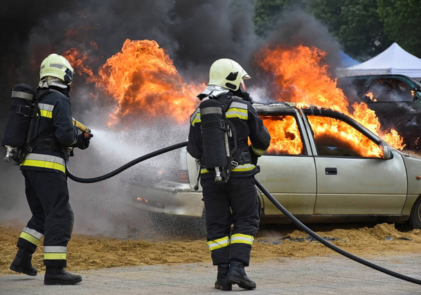 Bomberos en el trabajo junto a un coche en llamas - Foto, imagen