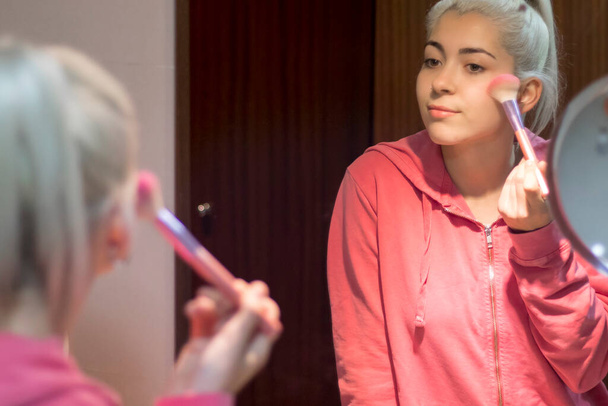 young girl applying makeup cosmetics early morning at home bathroom - Foto, afbeelding