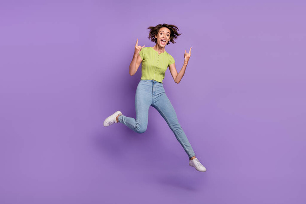 Photo of sweet rude young woman dressed green t-shirt jumping showing hard rock signs isolated purple color background. - Фото, изображение