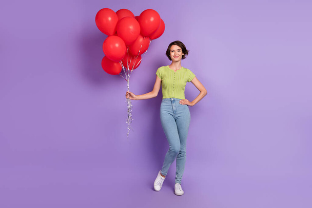 Photo of pretty adorable young woman dressed green t-shirt holding red air balls isolated purple color background. - Foto, Bild