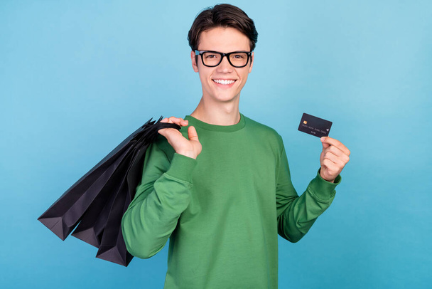 Photo portrait young guy smiling wearing green pullover glasses showing bank card on shopping isolated pastel blue color background. - Foto, immagini