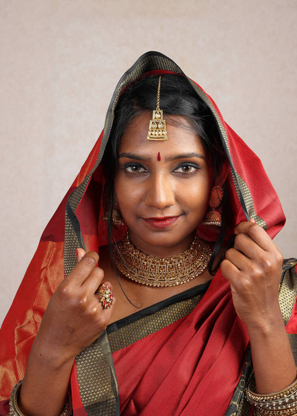 Indická žena na sobě červená oranžová saree šperky choker set náhrdelník jhumka náušnice maang tikka pas řetěz stojan póza pohled vidět úsměv nálada výraz hlava kryt hidžáb   - Fotografie, Obrázek