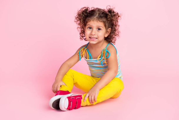 Portrait of attractive cute cheerful wavy-haired girl sitting on floor spending time isolated over pink pastel color background. - Foto, imagen