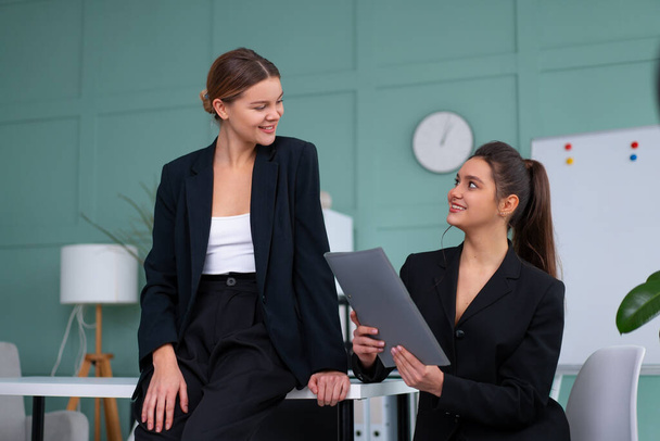 Young women leaders are checking financial statements from paper documents. Two female confident business worker dressed black suit in office checking financial document looking folder and discussing - Valokuva, kuva