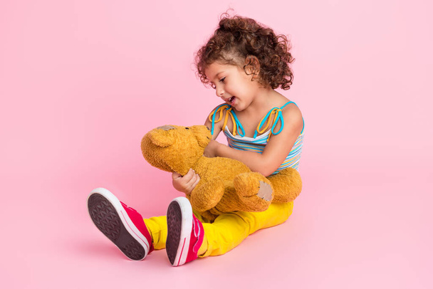 Portrait of attractive careful cheerful wavy-haired girl playing with old teddy bear isolated over pink pastel color background. - Foto, immagini