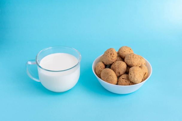 Овсяное печенье на белой тарелке, белое молоко в прозрачном стеклянном боковом виде на голубом фоне. Качественное фото - Фото, изображение