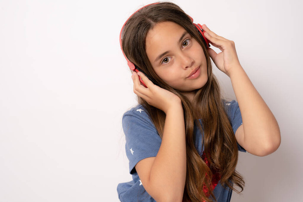 Beautiful modern girl singing favorite song, listening to music in wireless headphones standing over white background - Φωτογραφία, εικόνα