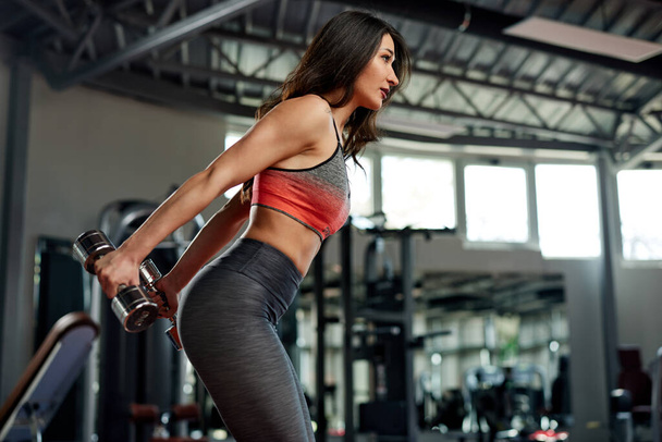Formda bir sporcu kadın spor salonunda göğüs ve kollar için dambıllarla egzersiz yapıyor.. - Fotoğraf, Görsel