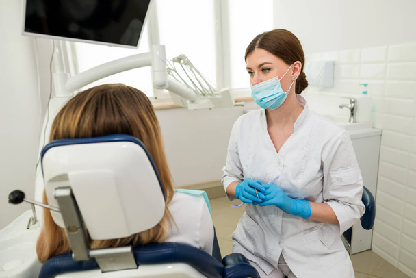 Een mooie vrouwelijke tandarts praat met een patiënt terwijl hij in een stoel zit. Toelichting, raadpleging, advies, aanbeveling van een tandarts - Foto, afbeelding