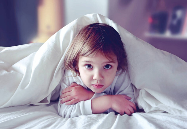 Child in bed under blanket. Kid bed time. Insomnia. Night mare. Little girl scared in bed. - Zdjęcie, obraz