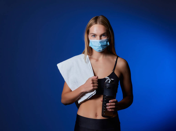 Atletische vrouw met gezichtsmasker ontspannen na het sporten in een fitnessruimte tijdens coronavirus epidemie. gezonde levensstijl en sportconcept. - Foto, afbeelding