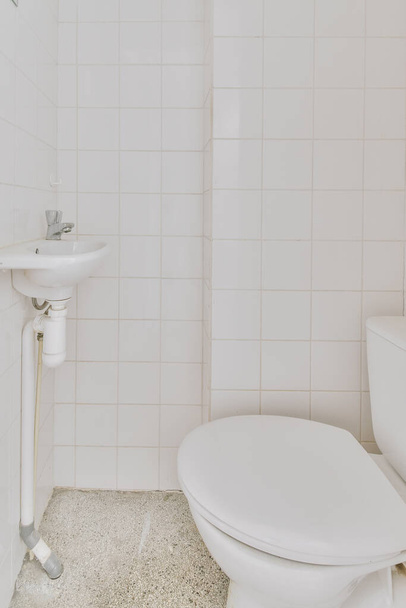Wnętrze wąskiej łazienki i WC z salonem, umywalką i toaletą ścienną z białymi ścianami i podłogą w kratkę - Zdjęcie, obraz