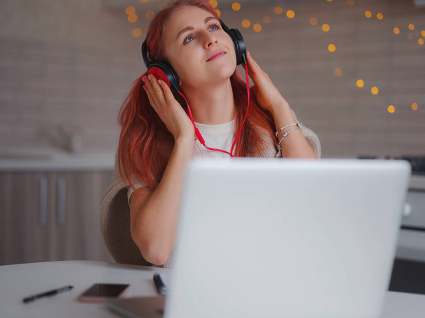 attractive young woman working with laptop in kitchen. casual lady enjoying in her favorite song over headphones and singing while working on laptop in home office. - 写真・画像