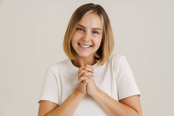 Young blonde woman smiling while holding her hands together isolated over white background - Photo, Image