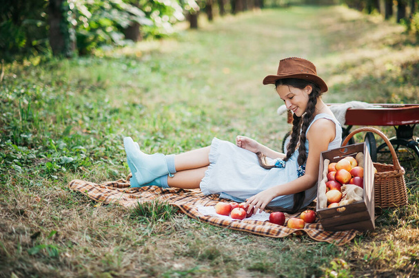 Girl with Apple in the Apple Orchard. Beautiful Girl Eating Organic Apple in the Orchard. Harvest Concept. Garden, Toddler eating fruits at fall harvest. - Photo, Image