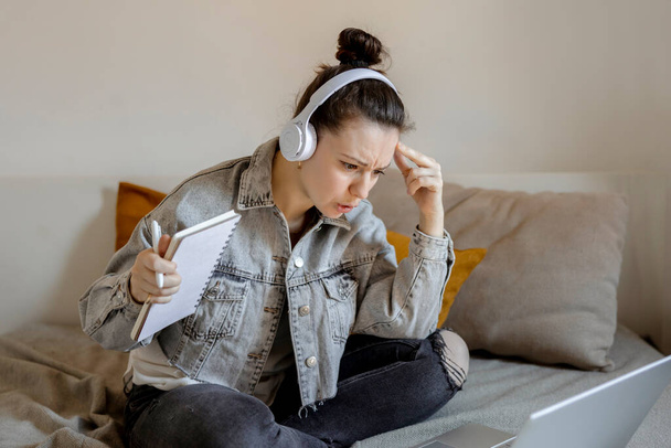 Angry and dissatisfied woman with casual clothes sitting on bed at home with computer and studying. Girl is sad and tired. Negative emotions, stress, mental problems, deadline. Distance education - Φωτογραφία, εικόνα
