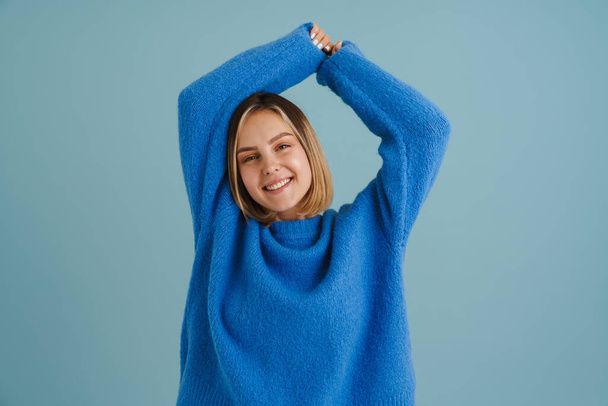 Young blonde woman smiling while posing with hands up isolated over blue background - Foto, immagini