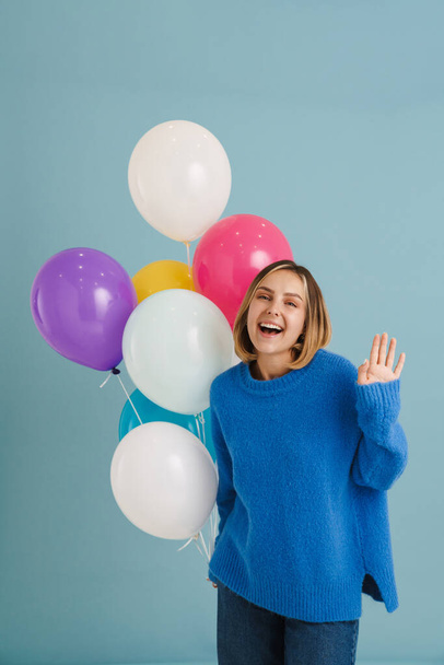 Young blonde woman gesturing while posing with balloons isolated over blue background - Foto, imagen