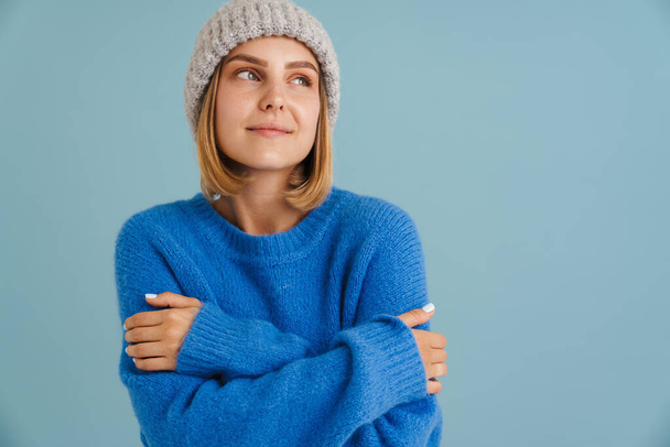Young blonde woman wearing knit hat smiling at camera isolated over blue background - Foto, Imagem