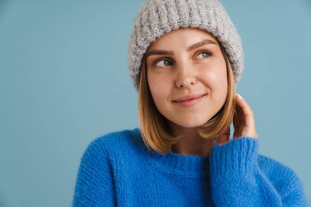 Young blonde woman wearing knit hat smiling at camera isolated over blue background - Φωτογραφία, εικόνα