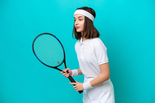 Young Ukrainian woman isolated on blue background playing tennis - 写真・画像