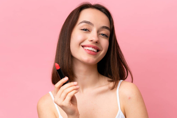 Young Ukrainian woman isolated on pink background holding red lipstick - Fotó, kép