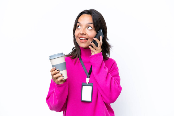 Young hispanic woman with ID card isolated on white background holding coffee to take away and a mobile - Photo, Image