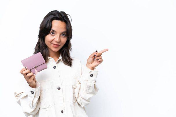 Young hispanic woman holding wallet isolated on white background pointing finger to the side - Фото, изображение