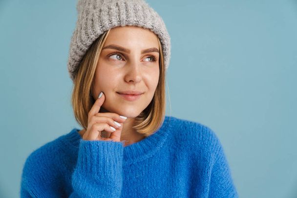 Young blonde woman wearing knit hat smiling at camera isolated over blue background - Фото, зображення