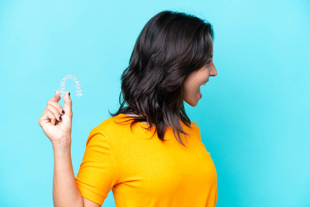 Young hispanic woman holding invisible braces isolated on blue background laughing in lateral position - Foto, immagini