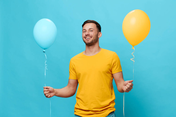 Sarı tişörtlü, mutlu gülümseyen yakışıklı adam diyor ki "Evet, mavi stüdyo arka planında izole edilmiş balonlar tutun". Uzayın afiş modelini kopyala. Arkadaşlık kavramı - Fotoğraf, Görsel