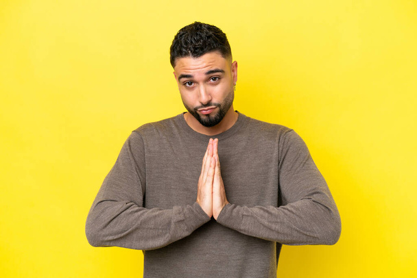 Young Arab handsome man isolated on yellow background keeps palm together. Person asks for something - Foto, Imagem