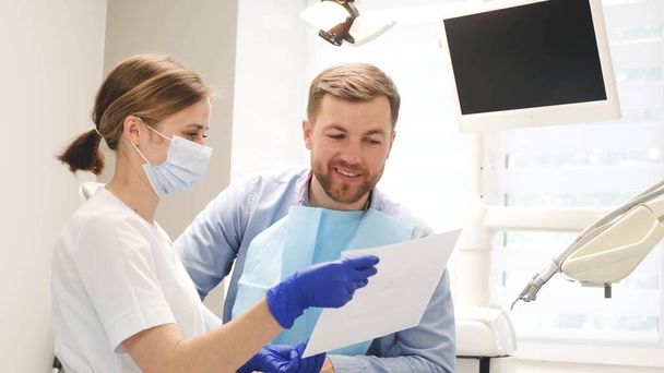 La doctora le muestra al paciente una radiografía de los dientes. El dentista se comunica con el cliente en una clínica dental moderna. Vídeo 4k - Foto, Imagen