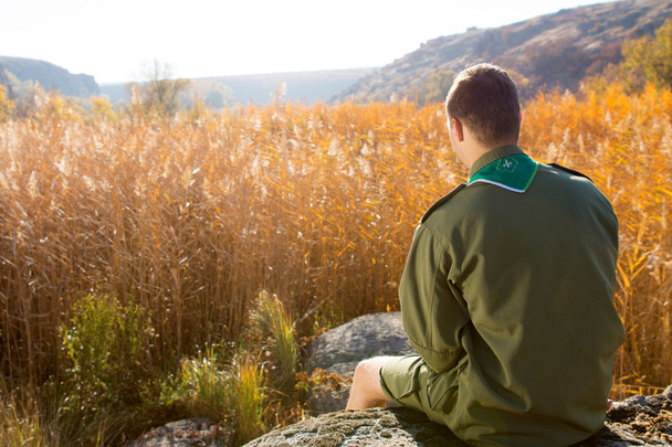 Boy Scout Sitting on the Rock Watching Brown Field - Fotoğraf, Görsel