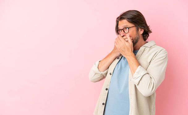 Sênior holandês homem isolado no fundo rosa cobrindo boca e olhando para o lado - Foto, Imagem