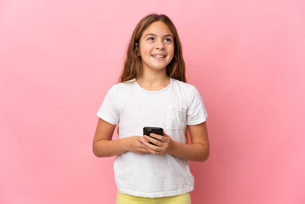 Child over isolated pink background using mobile phone and looking up - Photo, Image