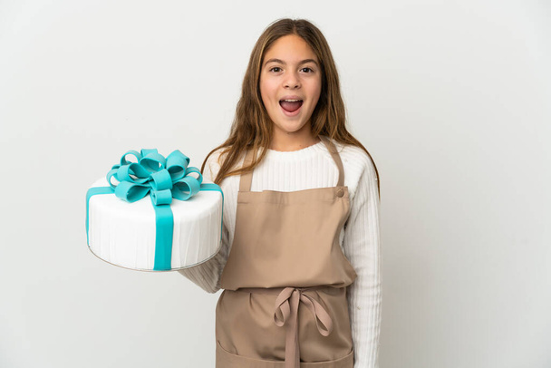 Little girl holding a big cake over isolated white background with surprise facial expression - Фото, зображення