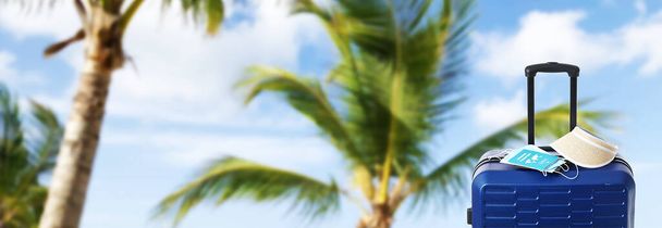 Чемодан путешественника, козырек, медицинская маска и иммунный паспорт на тропическом морском пляже. Баннер для дизайна - Фото, изображение