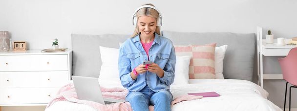 Mujer joven con smartphone escuchando música en el dormitorio - Foto, Imagen