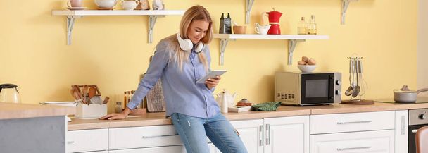 Hezká mladá žena se sluchátky a tabletu počítače v kuchyni - Fotografie, Obrázek